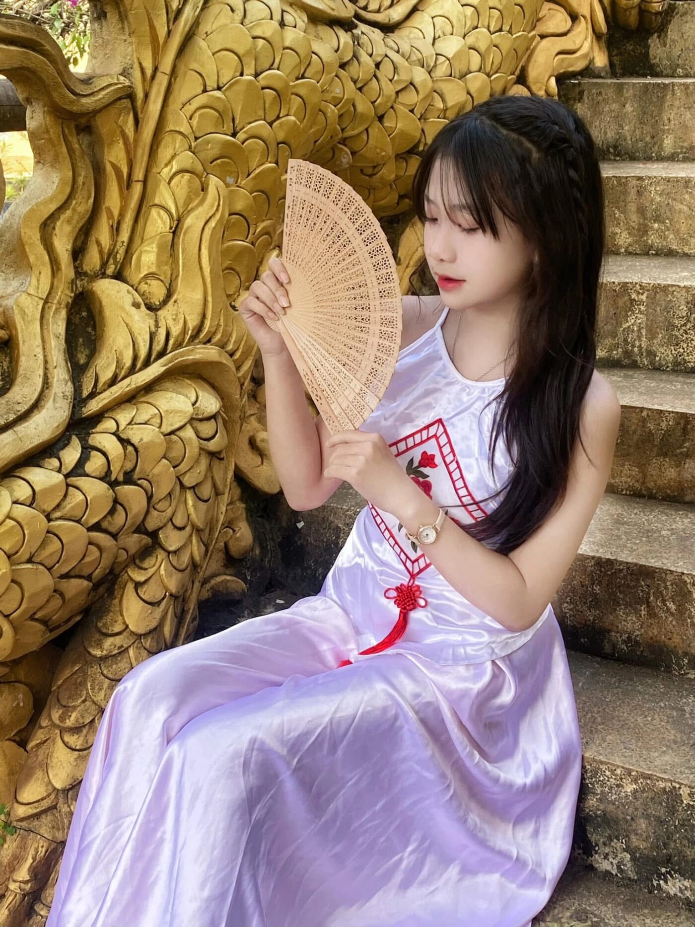 Tóc mái thưa uốn nhẹ, diện áo dài tím truyền thống, cầm quạt dịu dàng.