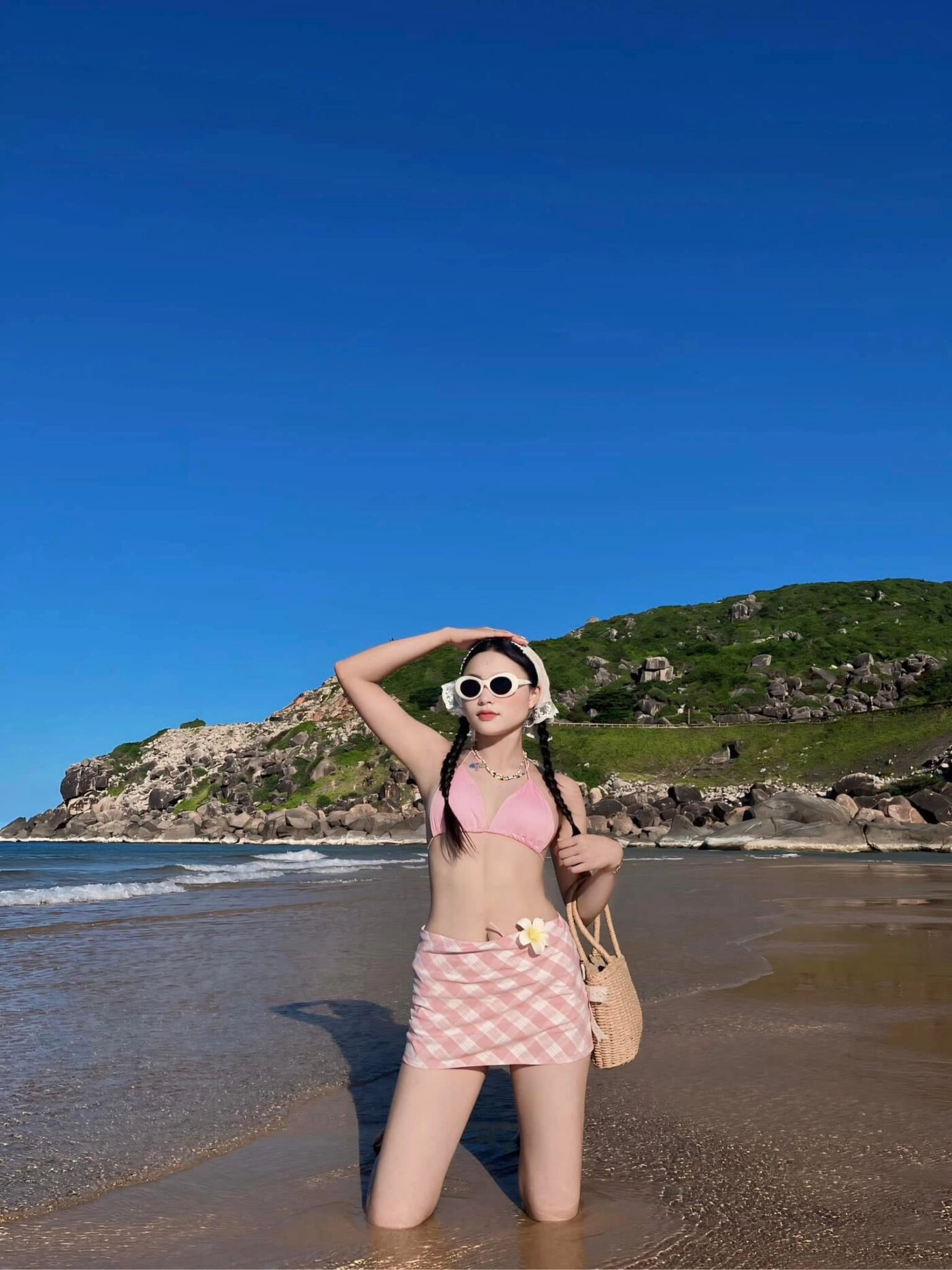 Bikini hồng kết hợp tóc tết hai bên và mắt kính tròn cá tính trên biển.